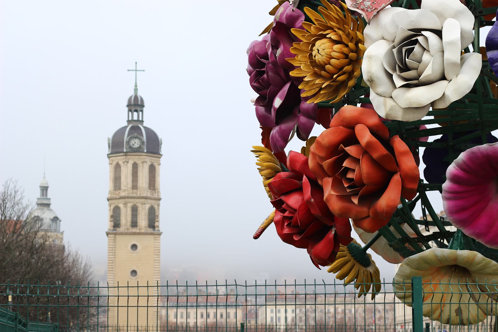 Gros plan sur les fleurs en acier peint de la sculpture, avec le clocher de l'Hôtel-Dieu en arrière-plan