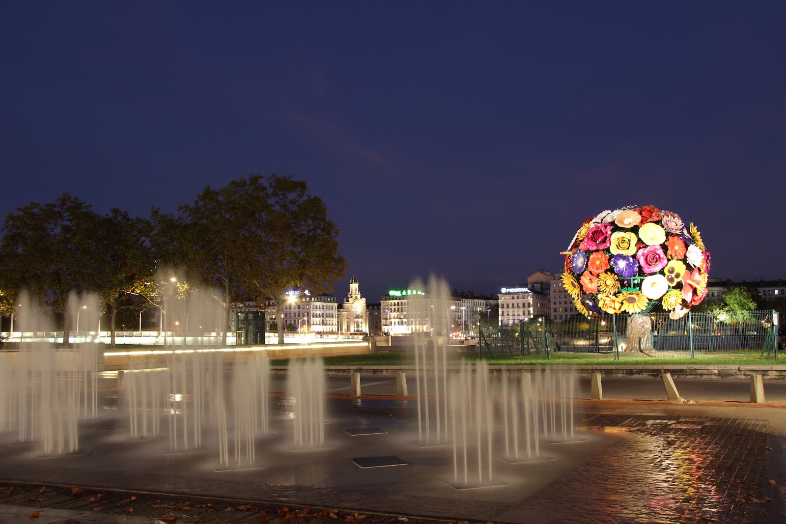 L'Arbre à Fleurs illuminé la nuit, au bord des jets d'eau de la fontaine d'Antonin Poncet